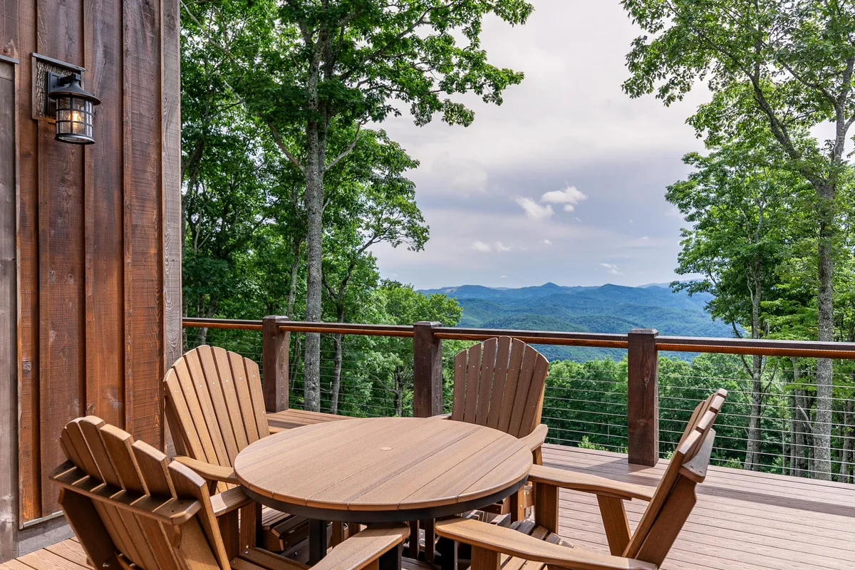 A cozy outdoor space featuring a wooden table surrounded by Adirondack chairs, framed by trees and a breathtaking mountain view. The setting is ideal for relaxing, dining al fresco, or sharing stories after a day of adventure.