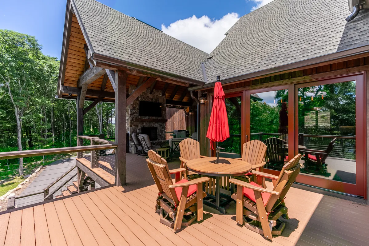 A welcoming outdoor scene with a wooden deck, red umbrella, comfortable seating area, and surrounding trees. The area is arranged for outdoor dining or casual group meetings, and the natural setting creates a sense of privacy and retreat.