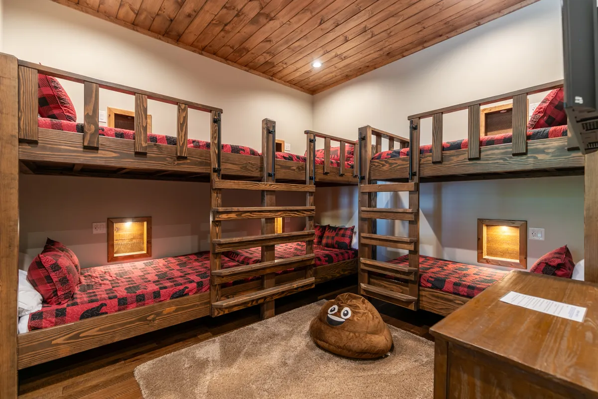 A playful and inviting bunkroom with multiple bunk beds decked in plaid bedding, a cozy bean bag chair, and ample space for play and relaxation. Bright and whimsical, perfect for children or groups.