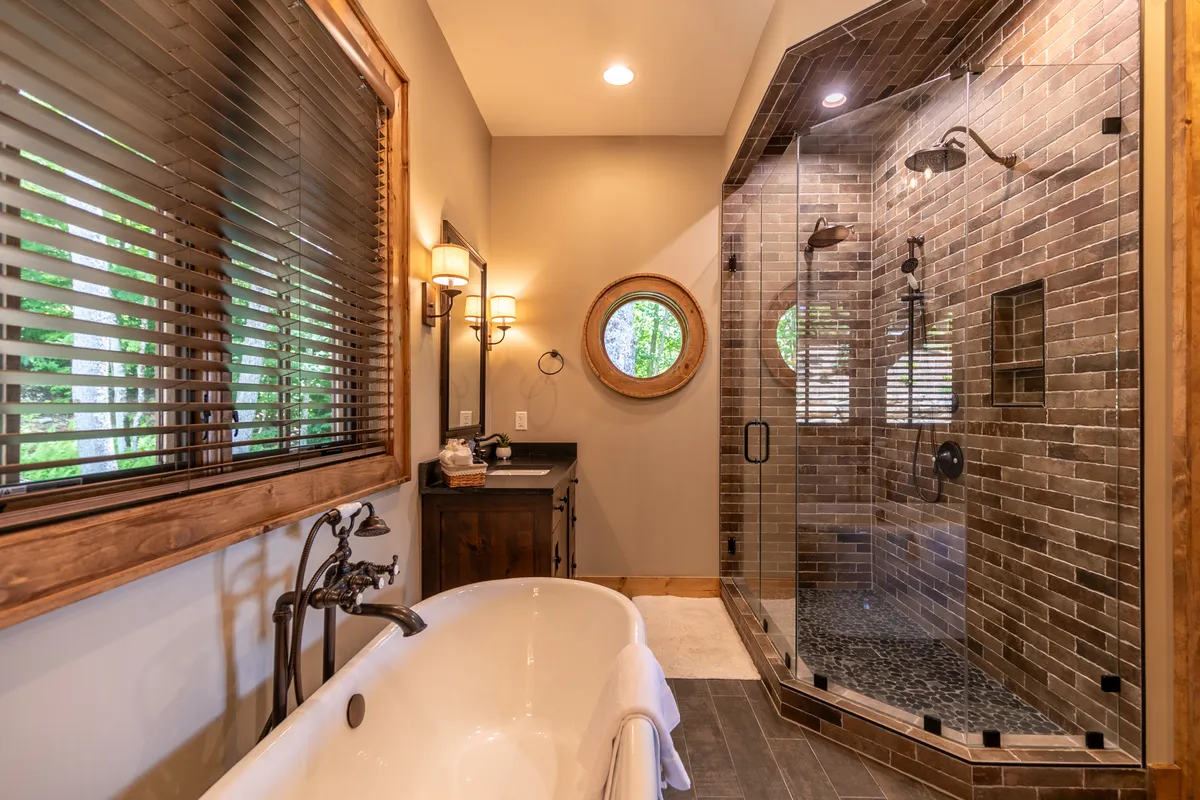 A luxury bathroom with a freestanding bathtub, glass shower, wooden accents, and a unique circular window, all designed for serene self-care. The space feels modern and tranquil, ideal for relaxation after mountain adventures.
