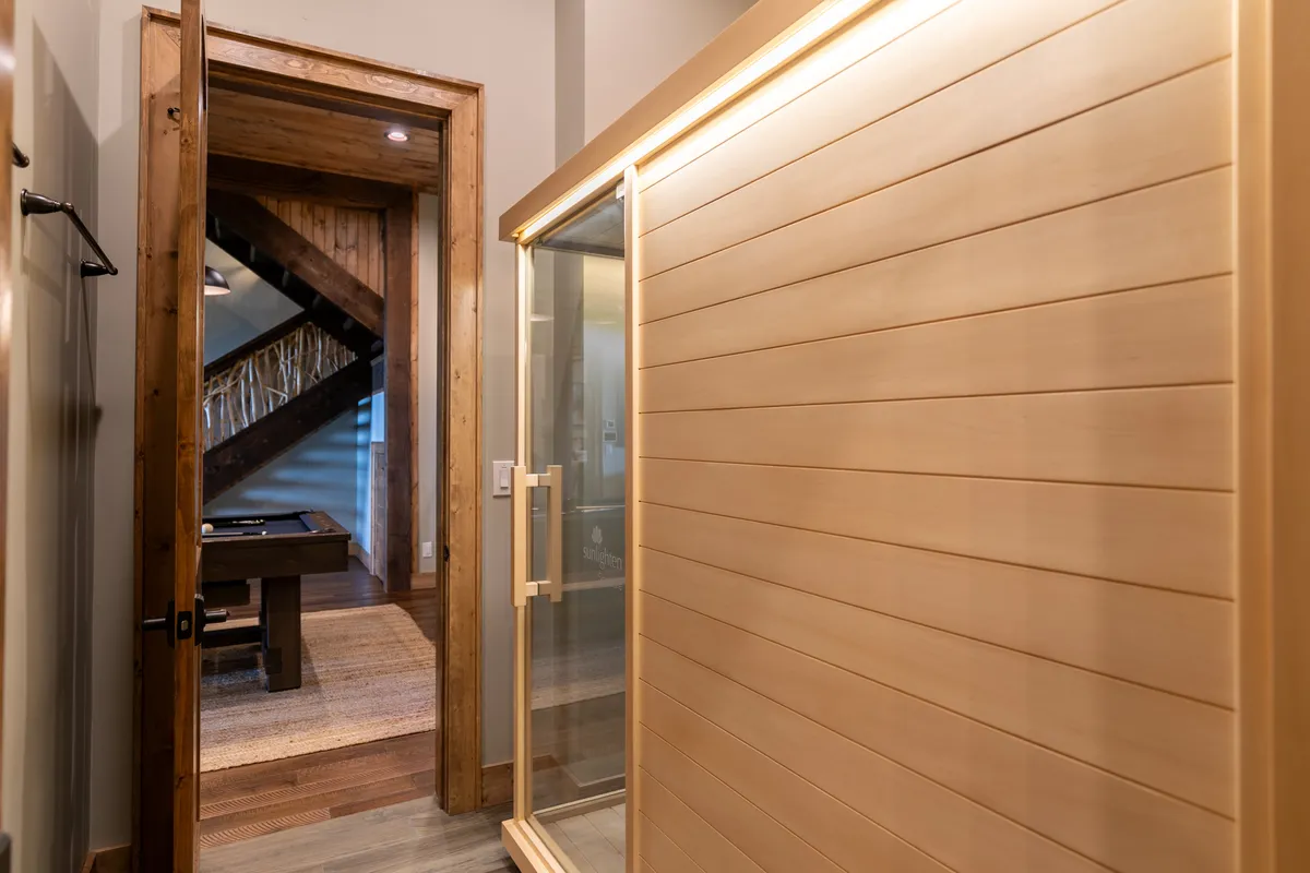 A serene corner featuring a sauna with wood paneling and a glass door, positioned near a wooden staircase in the home. The area exudes relaxation and wellness, providing a visual cue to the in-home spa and infrared sauna amenity.