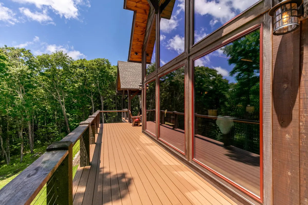 A wide exterior view of The Phoenix, featuring large windows and a spacious wooden deck surrounded by lush greenery. People are seen relaxing on the deck and enjoying the natural surroundings, suggesting a tranquil environment ideal for group interaction and unwinding.