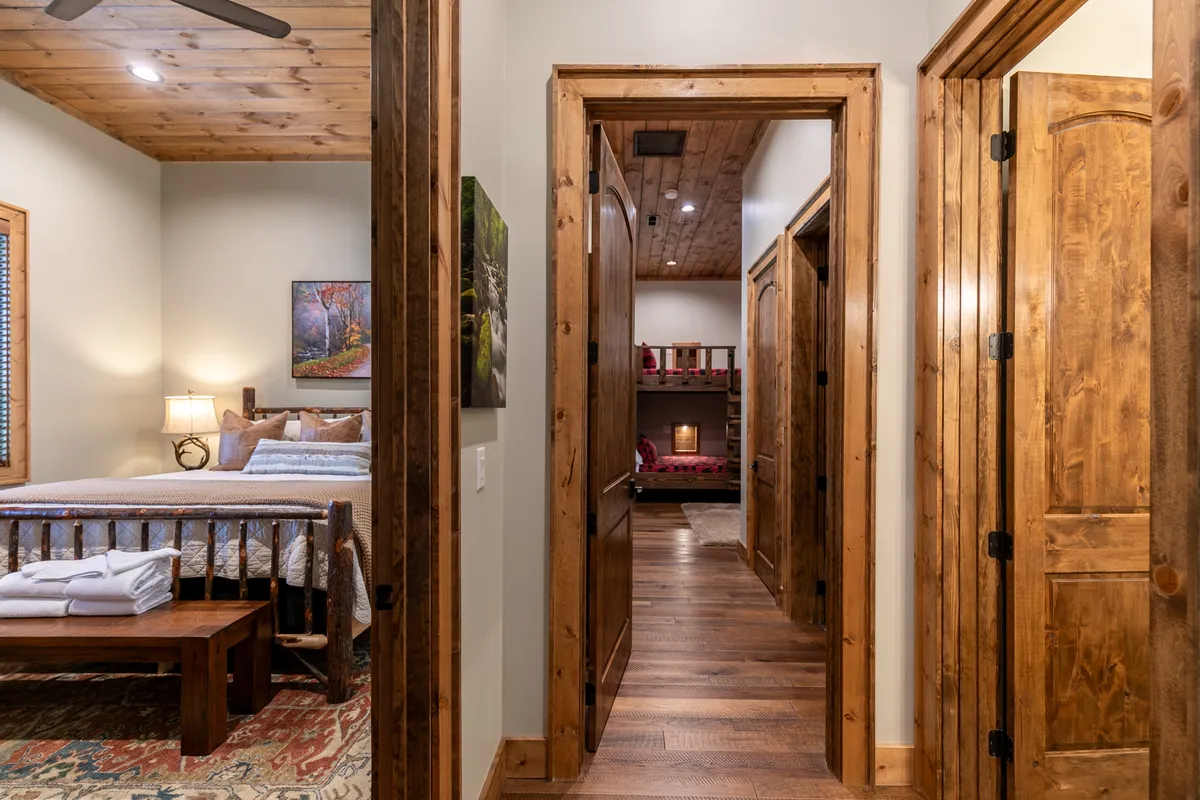 A flexible retreat above the garage featuring a bed with a patterned quilt, wooden furniture, artwork on the wall, and bunk beds in the background. The room feels inviting and adaptable for families or groups.